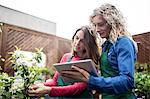 Two female florist using digital tablet while checking plants in garden centre