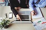 Mid section of businessman discussing with colleague over laptop in office