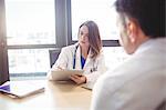 Female doctor sitting at her desk writing on clipboard in front of patient in the hospital