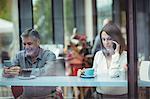 Man text messaging while woman talking on mobile phone in the cafeteria