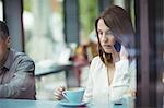 Woman holding coffee cup and talking on mobile phone in cafeteria