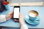 Close-up of woman text messaging on mobile phone in cafeteria