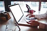 Woman holding mobile phone and using laptop in the office