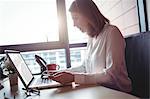 Woman holding mobile phone and using laptop in the office