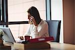 Woman using laptop and talking on mobile phone in the office