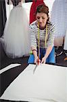 Female fashion designer cutting a white fabric in the studio