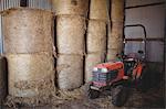 Stack of hay bales and tractor in barn