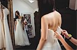 Woman trying on wedding dress in a studio with the assistance of creative designer