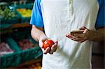 Man holding tomato and using phone while shopping in supermarket