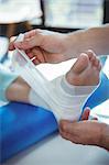 Male therapist putting bandage on female patient foot in clinic