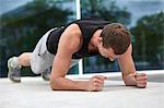 Young man training in city, doing elbow push ups