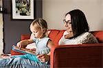 Mother teaching daughter to read book on sofa