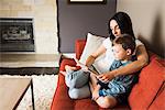 Mother teaching son to read book on sofa