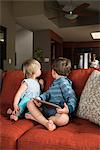 Siblings turning around from digital tablet on sofa