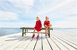 Two young friends sitting on bench on wooden pier