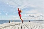 Young girl on wooden pier, jumping to reach bubbles