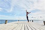Young boy on wooden pier, jumping to reach bubbles