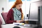 Young female college student at computer desk reading paperwork