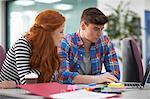 Young female and male college students looking at laptop on desk