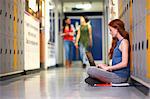 Young female college student sitting on locker room floor typing on laptop