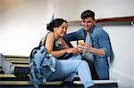 Young college student couple reading smartphone texts on stairway