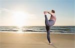 Mature woman practising yoga on a beach at sunset, tree pose