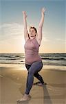 Mature woman practising yoga on a beach at sunset, warrior pose