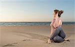 Mature woman practising yoga on a beach at sunset, sitting cross legged