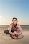 Mature woman practising yoga on a beach at sunset, portrait touching toes