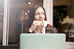 Businesswoman with laptop drinking espresso at sidewalk cafe