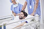 Doctors pushing smiling patient in hospital bed