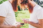 Young male hipster twins with red beards opposite each other texting on smartphones