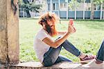 Young male hipster with red hair and beard photographing friend on smartphone in park