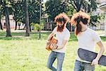 Young male hipster twins with red hair and beards strolling in park playing guitar