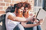 Young male hipster twins with red hair and beards browsing digital tablet on sidewalk