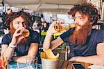Young male hipster twins with red hair and beards drinking beer at sidewalk bar