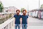 Portrait of young male hipster twins with red hair and beards standing on bridge