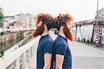 Portrait of young male hipster twins with red hair and beards back to back on bridge