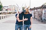 Portrait of two men wearing rabbit and horse masks on urban bridge