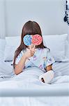 Portrait of girl patient holding lollipops in front of her eyes in hospital children's ward