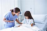 Female nurse explaining to girl patient with arm plaster cast in hospital children's ward