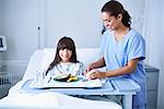 Female nurse serving lunch to girl patient with arm plaster cast in hospital children's ward