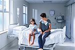 Girl patient and her mother sitting on bed in hospital children's ward