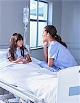 Nurse talking with girl patient sitting up in bed on hospital children's ward