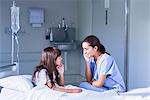 Nurse talking with girl patient sitting up in bed on hospital children's ward