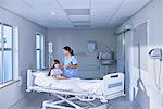 Nurse adjusting intravenous drip for girl patient in bed on hospital children's ward