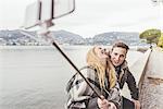 Young couple laughing taking smartphone selfie on harbour wall, Lake Como, Italy