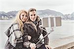 Young couple taking smartphone selfie on harbour wall, Lake Como, Italy