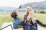 Young couple on picnic blanket blowing and photographing bubbles,  Lake Como, Italy