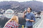 Young couple on waterfront blowing bubbles,  Lake Como, Italy